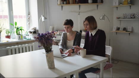 Zwei-Junge-Frauen-Sitzen-Am-Tisch-Und-Nutzen-Ein-Notebook-Für-Die-Online-Bestellung