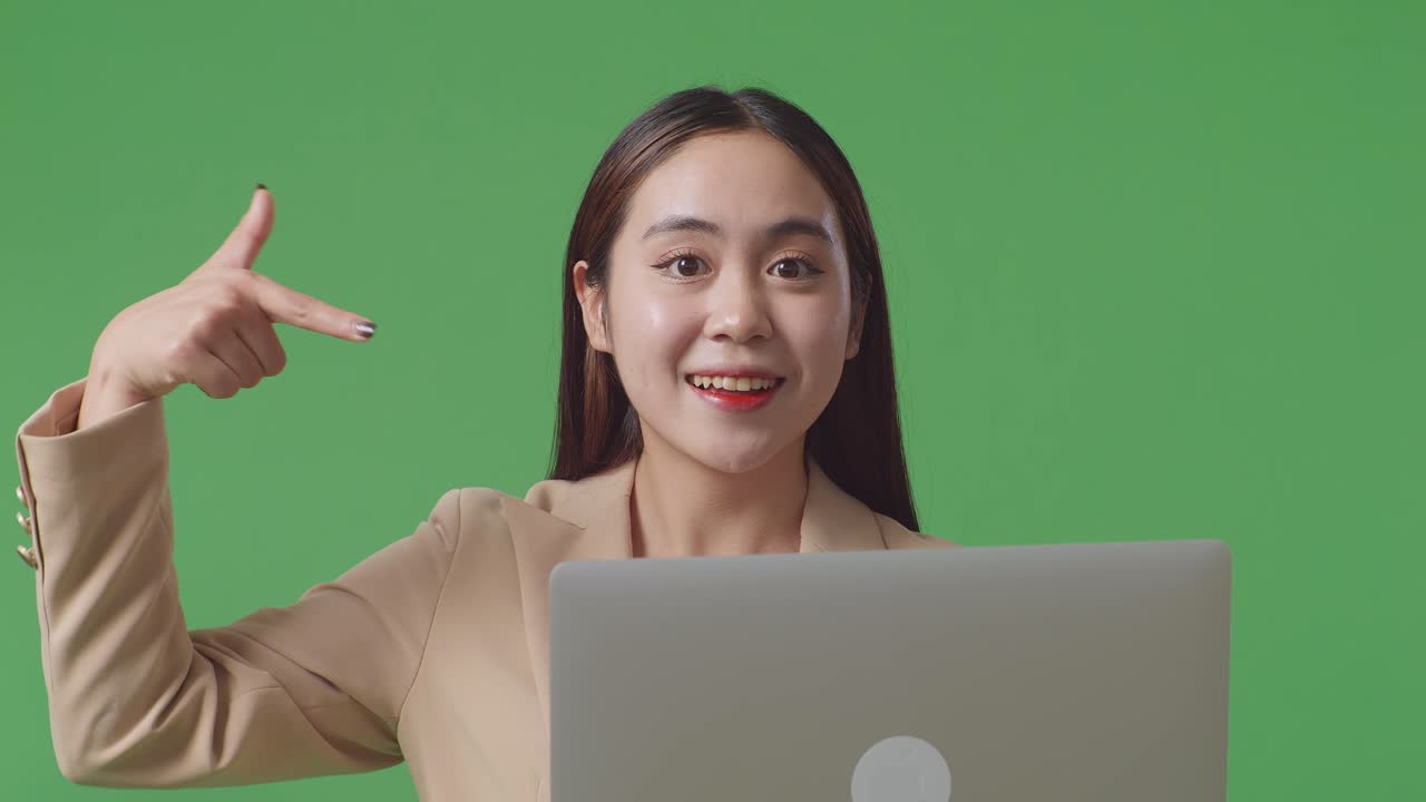 스튜디오에서 녹색 화면 배경에 노트북 컴퓨터를 사용하고 가리키는 동안 미소 짓는 아시아 사업가의 클로즈업