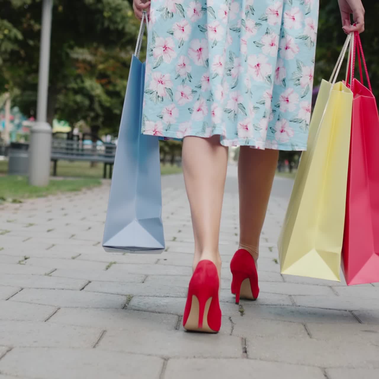 una mujer con zapatos rojos de tacón alto lleva bolsas de compras