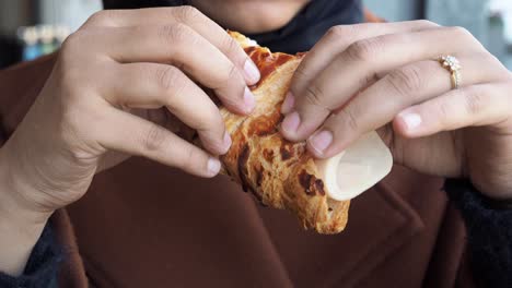 una mujer comiendo un sándwich de croissant.