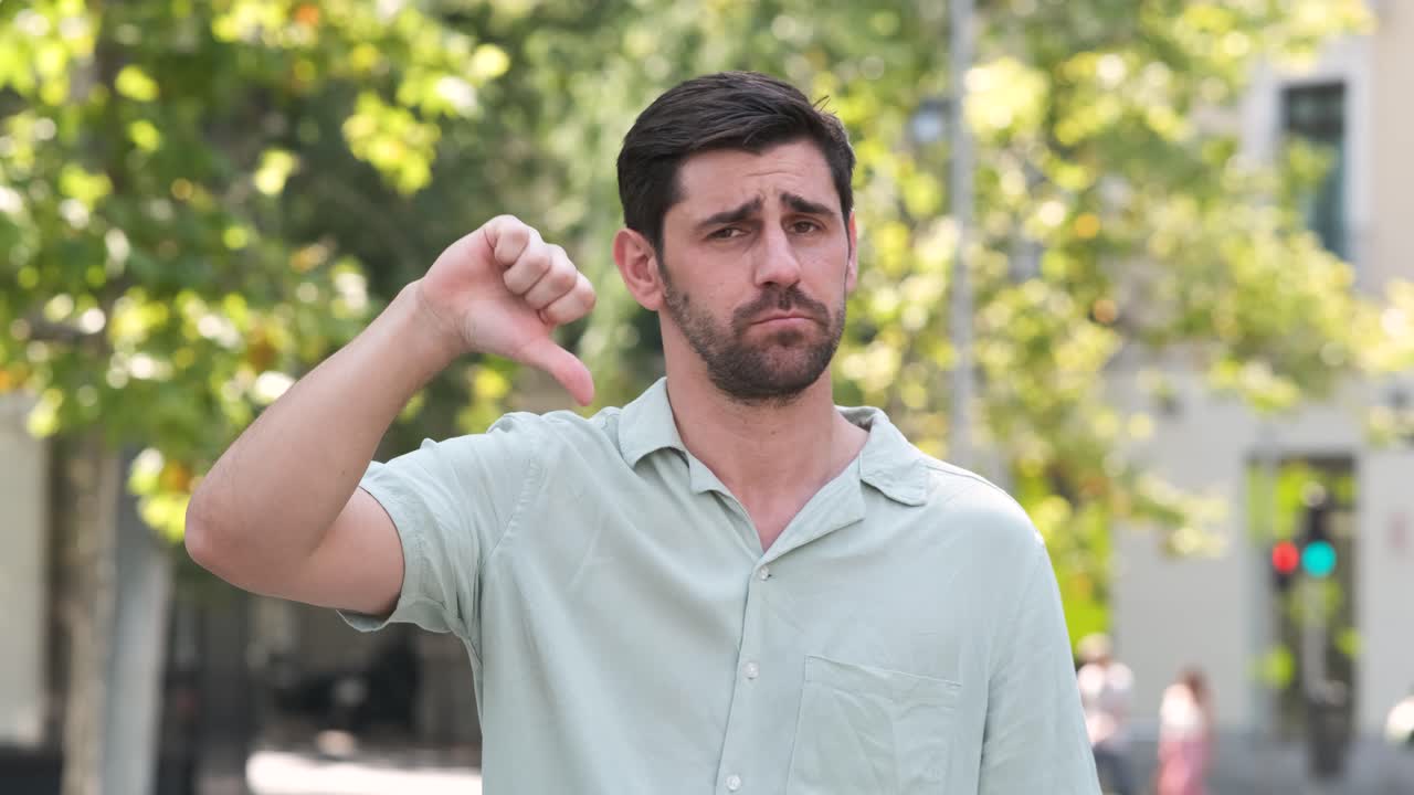 Dissatisfied man showing thumbs down at city park during daytime