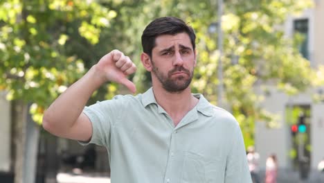 dissatisfied man showing thumbs down at city park during daytime