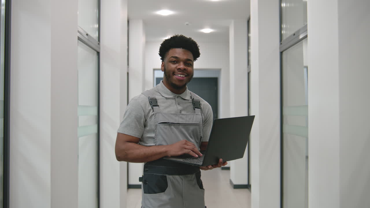 trabalhador afro-americano sorridente no corredor do escritório com laptop