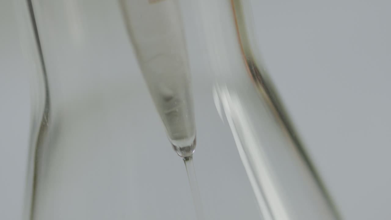 Detailed close-up of a liquid pouring from a measuring cylinder into a flask in a laboratory setting.