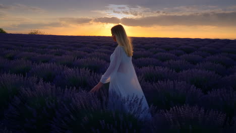 woman in white dress walking through a lavender field at sunset