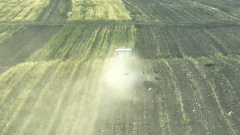 Siguiente-Toma-Aérea-De-Pájaros-Volando-Detrás-Del-Tractor-En-El-Campo-Y-Polvo-En-El-Aire