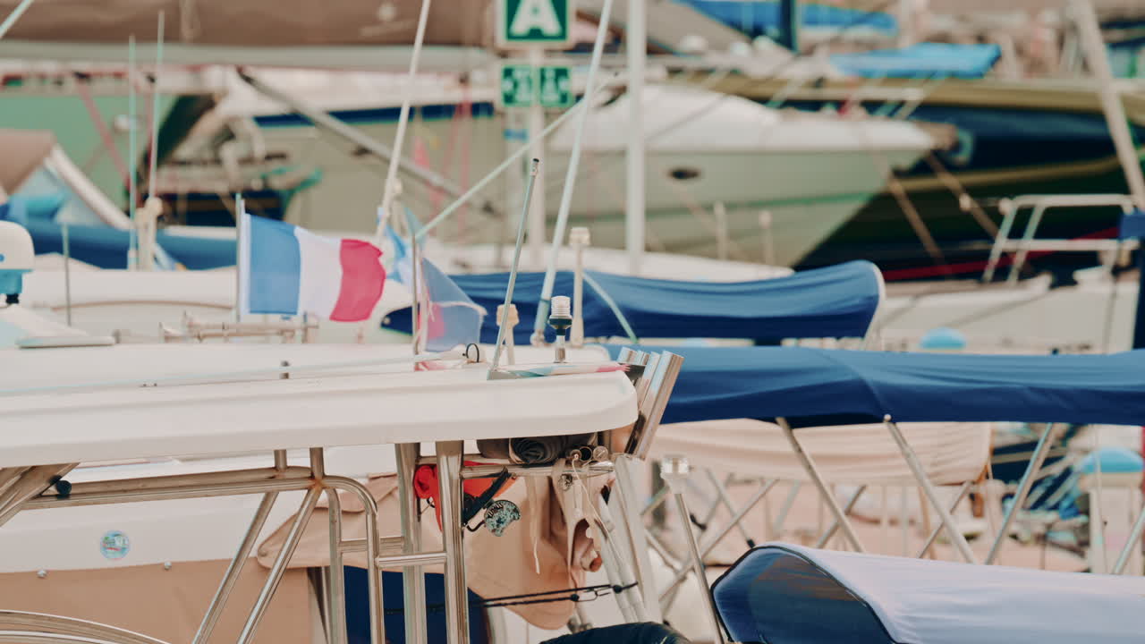 A busy marina filled with sailboats, sun canopies and French flags, creating a layered pattern of blue and white tones