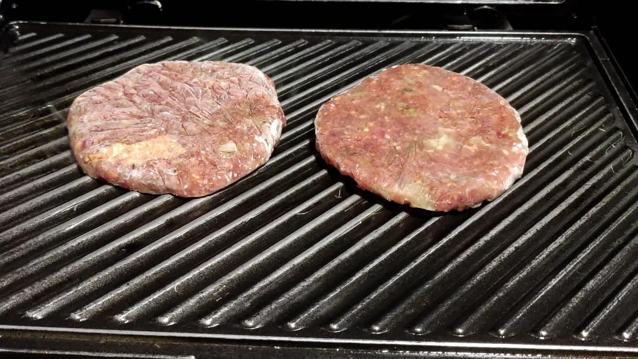 two hamburgers cooking on a black grill