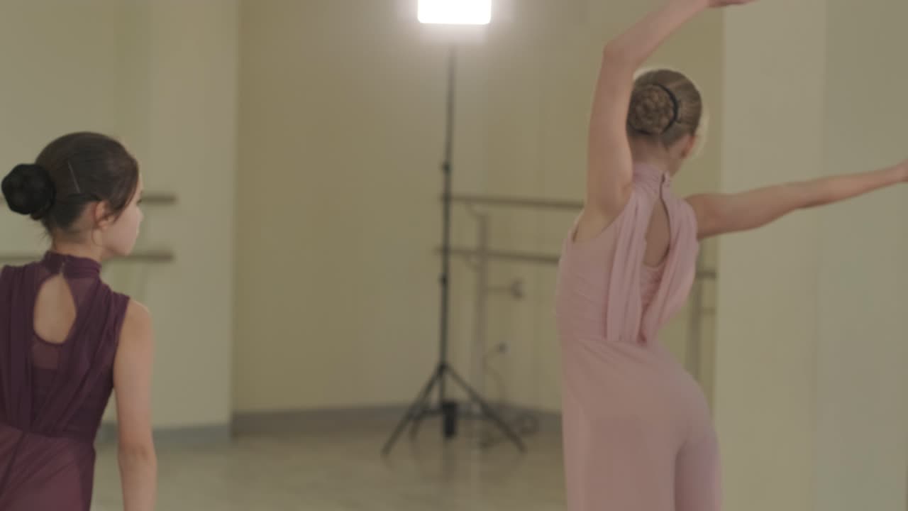 un grupo de jóvenes estudiantes de ballet con ropa de baile negra practicando posiciones en un amplio estudio de ballet con pisos de madera y barras montadas en la pared. expresiones enfocadas y movimientos sincronizados.