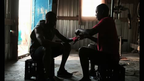 African-American-male-trainer-assisting-boxer-in-wearing-hand-wrap-in-gym-4k