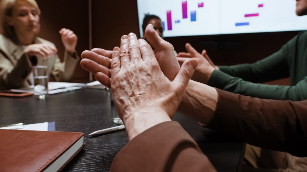 Business Team Clapping Hands in Meeting with Graphs on Screen