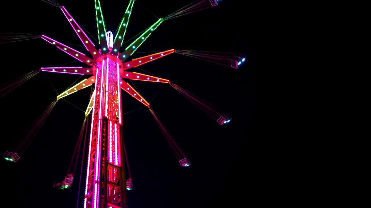 video en 4k de un paseo en una torre oscilante, también conocida como oscilante vertical y torre voladora cubierta con luces led multicolores que giran en el fondo del cielo negro de la noche oscura.