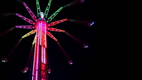 4k video of a swing tower ride, also known as vertical swing and flying tower covered with multicolored led lights spinning on the dark night black sky background.