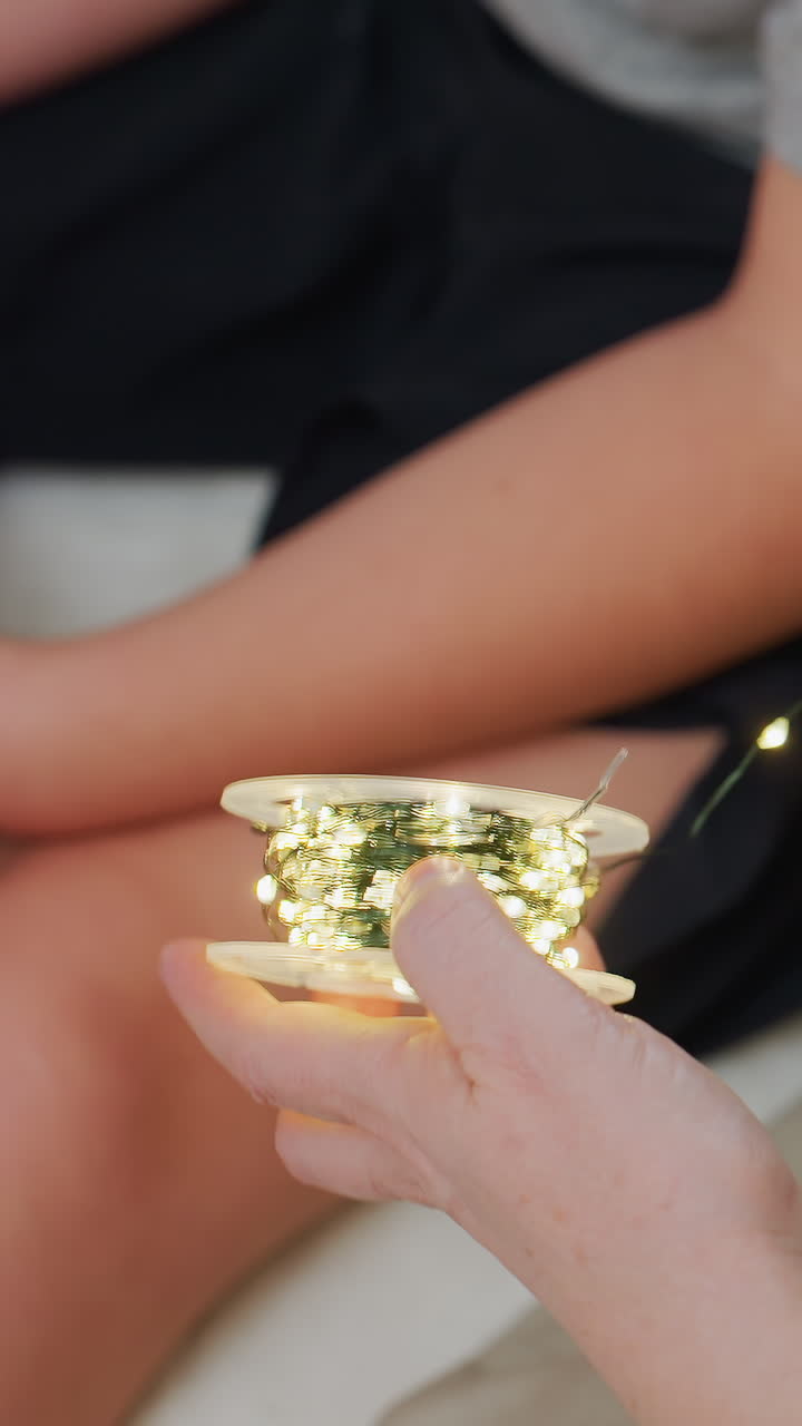 어른의 손이 아이에게 빛나는 요정 전구를 건네주고, 부드러운 침구 위에서 가까이 상호 작용하는 모습이에요. 작은 전구 뭉치가 무릎에 함께 놓여 있고, 호기심 가득한 손가락은 따뜻한 빛을 살펴보고 있죠. 장난기 넘치는 취침 시간의 유대감과 부드러움이 느껴져요.