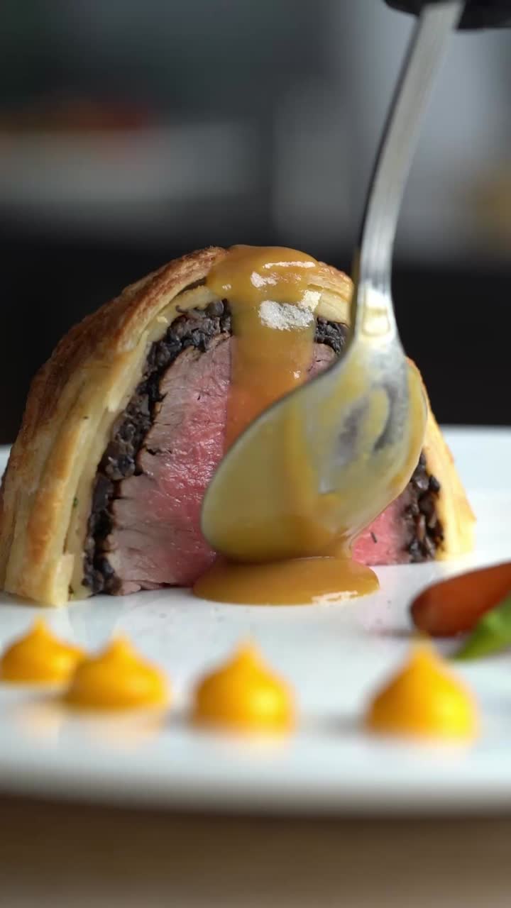 Uno chef versa la salsa su fette di Beef Wellington, primo piano, inquadratura di inserto