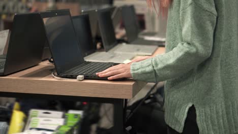 mujer elige una computadora portátil en una tienda de dispositivos