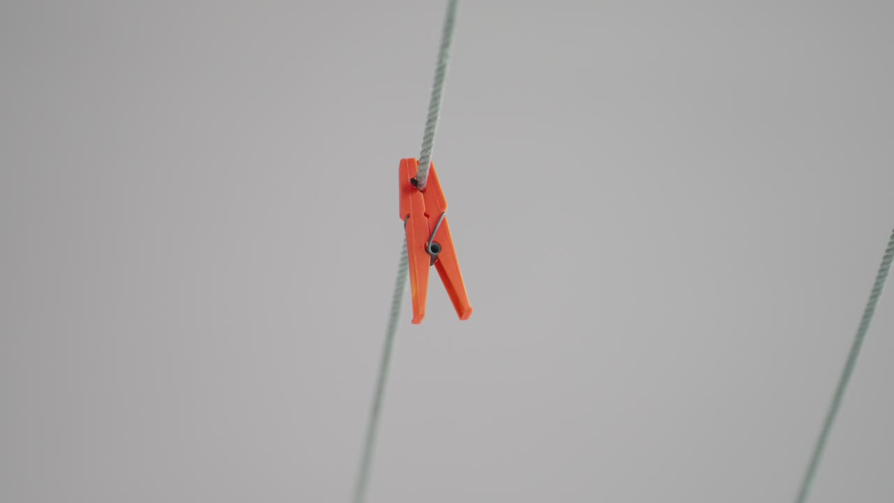 Close up of an orange clothespin on a rope against a gray background