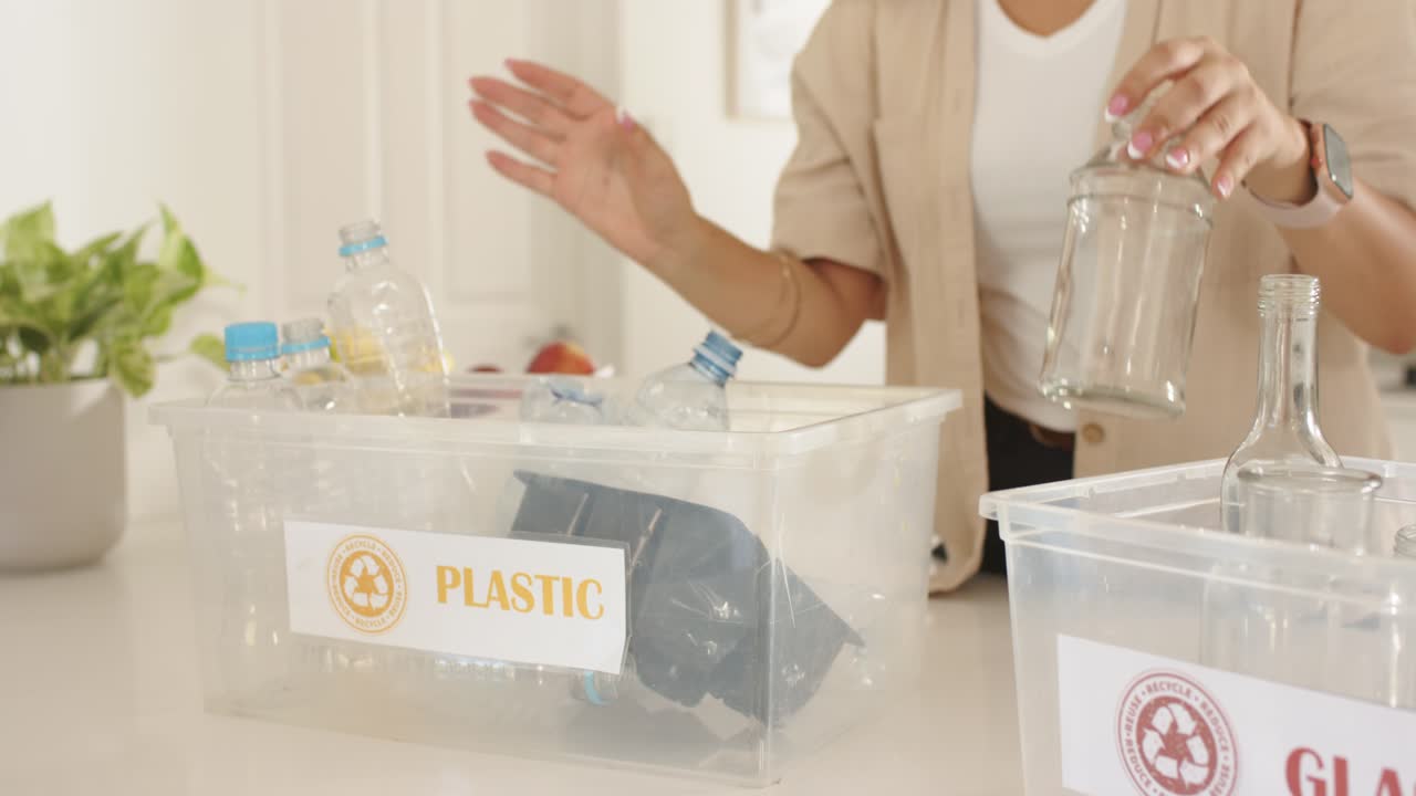 Mid-adult woman spotting bottle at counter, picking bottles into bins PLASTIC and GLASS, recycling