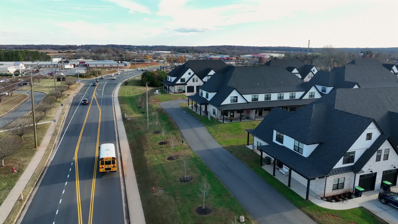 Peaceful American suburban with large modern homes, open green lawns and yellow school bus driving along wide roadway under clear skies. Peaceful autumn sunset. Aerial tracking shot