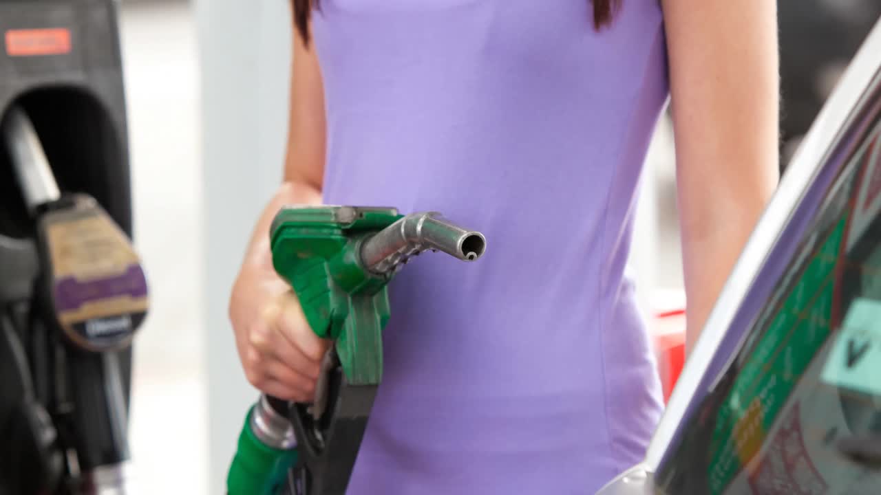 유리색  ⁇ 을 입은 백인 여성의 중간 부분은 주유소에서 연료  ⁇ 프를 채우는 차를 들고 있습니다.