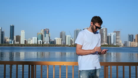 Bearded-traveler-in-sunglasses-booking-tickets-online-on-phone-connected-to-4G-internet-walking-with-coffee-streets-of-architectural-city.Tourist-with-vintage-camera-on-neck-reading-sms-on-cellular.