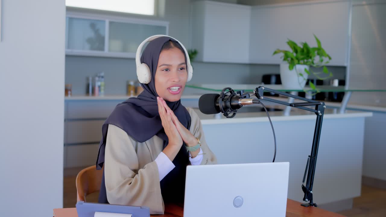 Voksen kvindelig vært justerer mikrofon, tager hovedtelefoner på, tjekker bærbar computer, optager podcast i køkkenet.