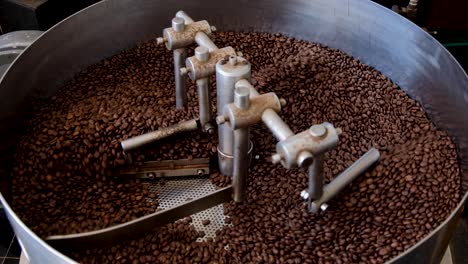 Industrial-professional-coffee-roaster-with-freshly-roasted,-aromatic-and-golden-brown-coffee-beans-cooling-in-turning-tray-at-local-coffee-shop