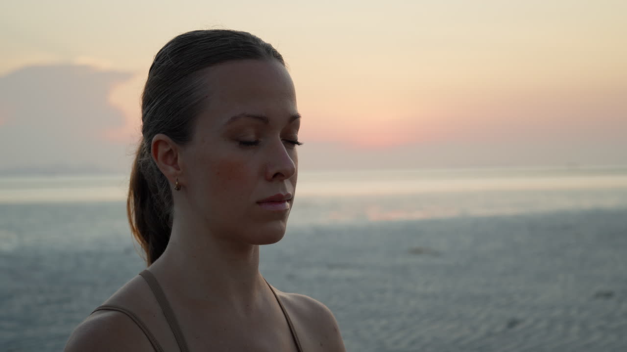 Young Woman Meditating with Eyes Closed on Beach at Sunset