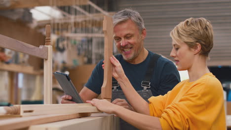 female apprentice learning from mature male carpenter with digital tablet in furniture workshop