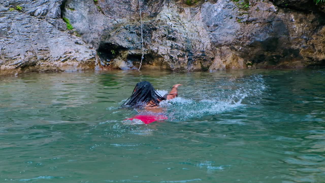 un hombre de pelo largo y piel oscura nadando en aguas turquesas cerca de la cascada - plano medio
