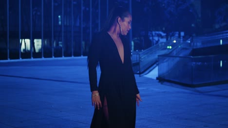 Sexy-latina-woman-walking-in-the-in-the-city-in-a-black-dress-with-blue-lights-in-the-background