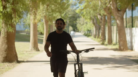 front view of man with bionic leg walking with bicycle in park