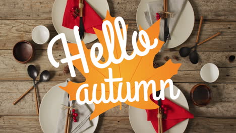 Animation-of-hello-autumn-text-over-cutlery-and-autumn-leaves-over-wooden-background