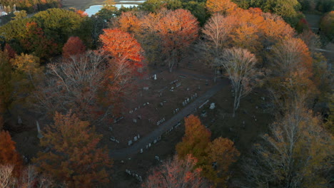 Toma-Aérea-De-Un-Cementerio-Rodeado-De-Coloridos-árboles-De-Otoño,-Puesta-De-Sol