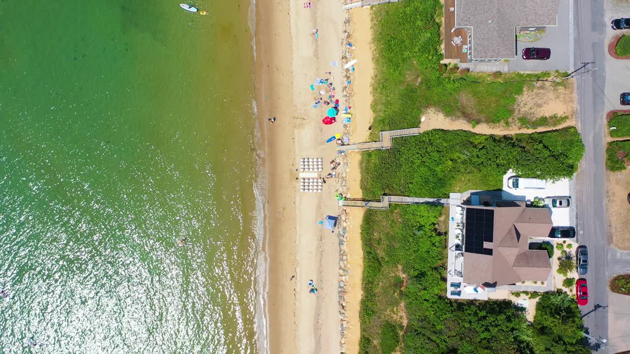 Nantucket aerial drone perspective highlights rows of seaside homes, lush green backyards, and wooden staircases connecting private properties directly to the sandy shoreline
