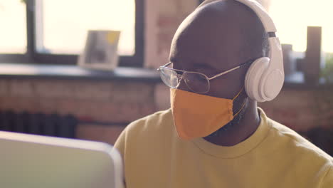 portrait of an man with headphones and face mask working on computer in an animation studio