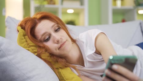 mujer acostada en casa mirando su teléfono aburrida.
