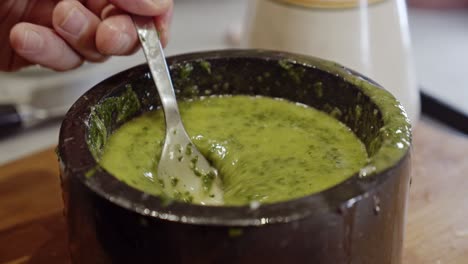 stirring healthy sauce with herbs in a ceramic black bowl with a metal spoon