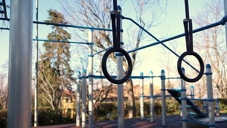 gymnastic rings move in the wind with trees and calisthenics structure on the background, steady close up shot