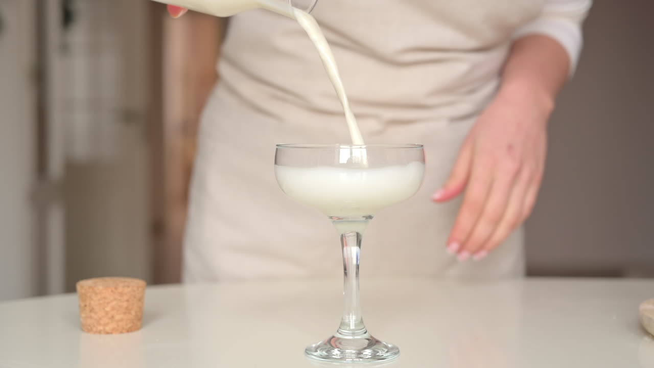 Mujer con un delantal sirviendo leche en una copa de cóctel en la cocina