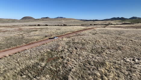 Drone-shot-of-car-driving-on-dirt-road-in-Willcox,-Arizona,-rising-aerial-shot