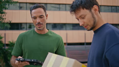 cheerful postman delivering box to customer in modern business district closeup