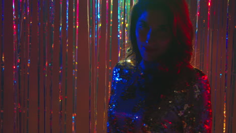 portrait of woman having fun in nightclub or bar dancing against sparkling tinsel curtain in background