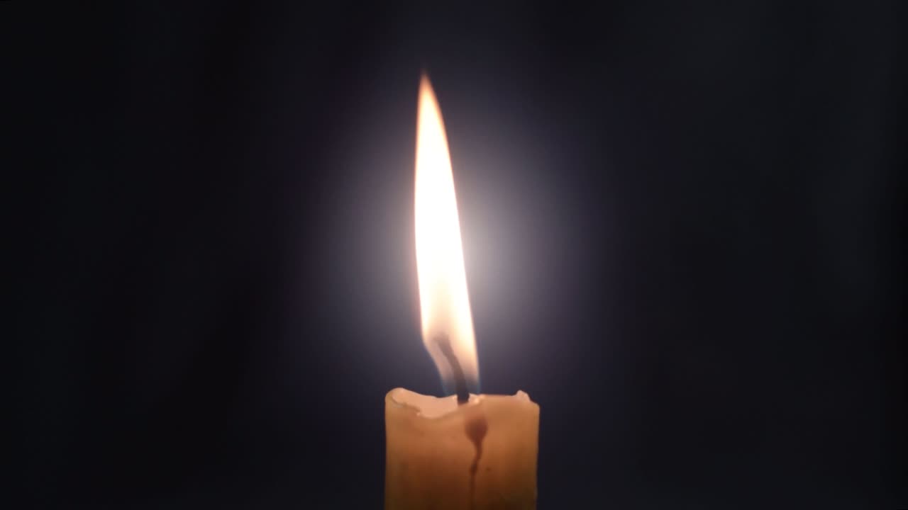 Semplice fiamma di candela tremolante su sfondo scuro