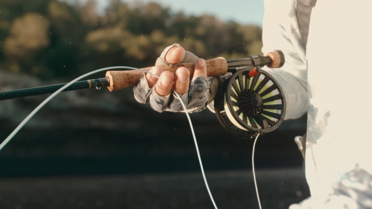 Extreme slow motion closeup of fly fisherman’s gloved hand pulling fishing line through fingers, droplets falling as line tightens during river angling