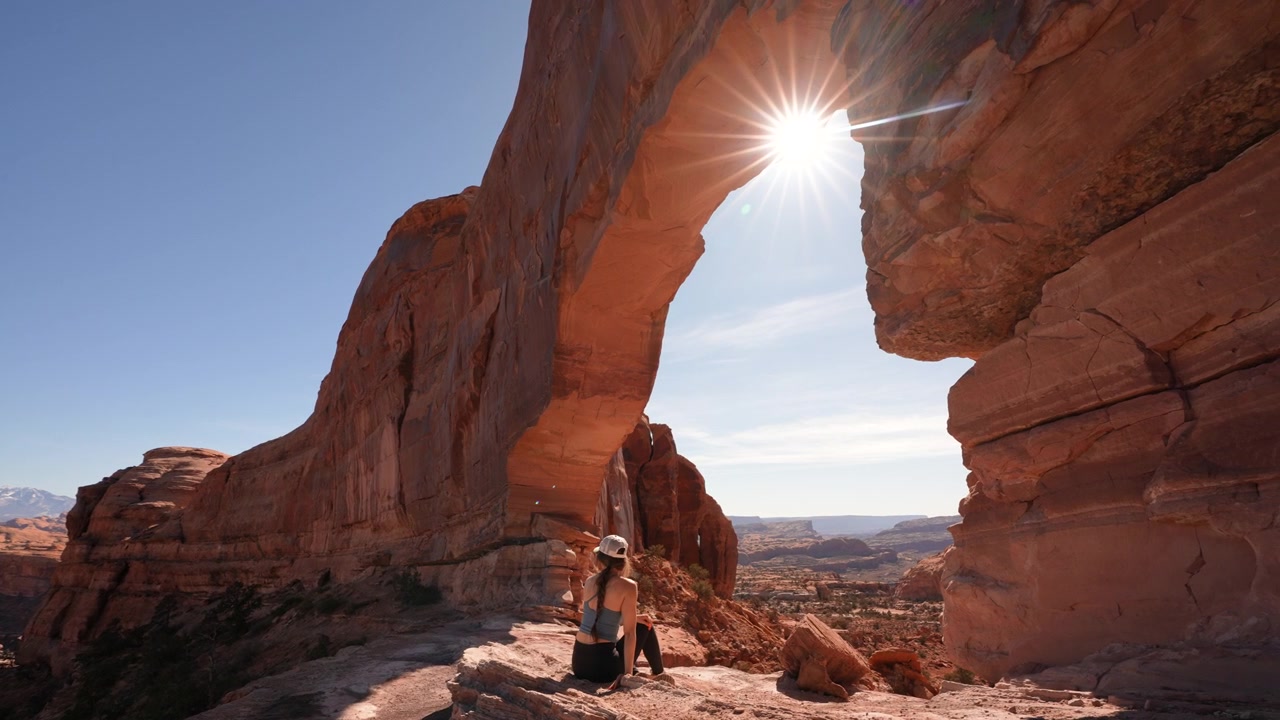 Donna seduta sotto un magnifico arco naturale nel paesaggio del deserto dello Utah. Jeep Arch vicino a Moab, USA