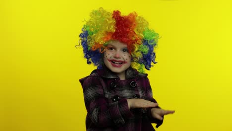 una niña payasa con una peluca arco iris haciendo caras tontas. divirtiéndose, sonriendo, bailando. halloween