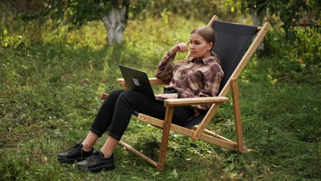 freelancing young lady working on laptop in the garden. lady stops for a moment to think over something and then continues work happily.