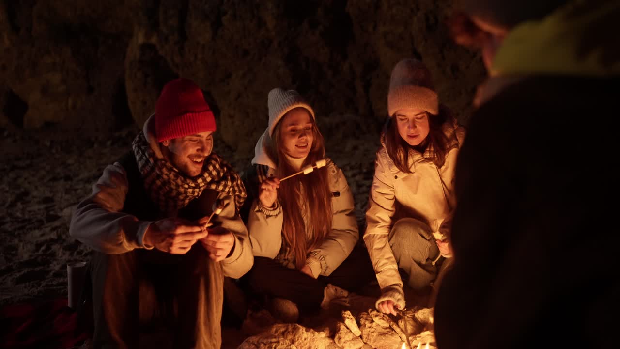 Friends roasting marshmallows by a campfire at night.