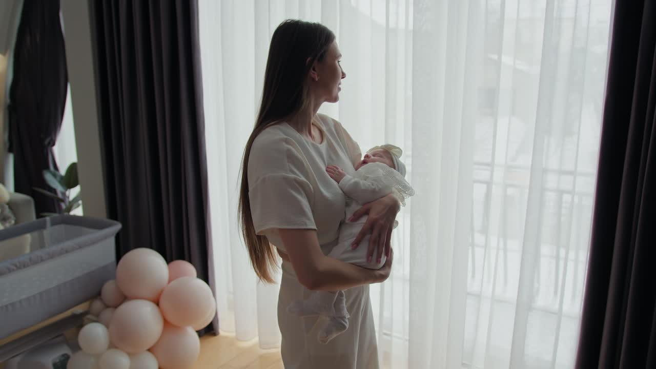 Mujer acuna a un bebé recién nacido cerca de la ventana, cortinas transparentes y cortinas oscuras, la suave luz del día ilumina la serenidad